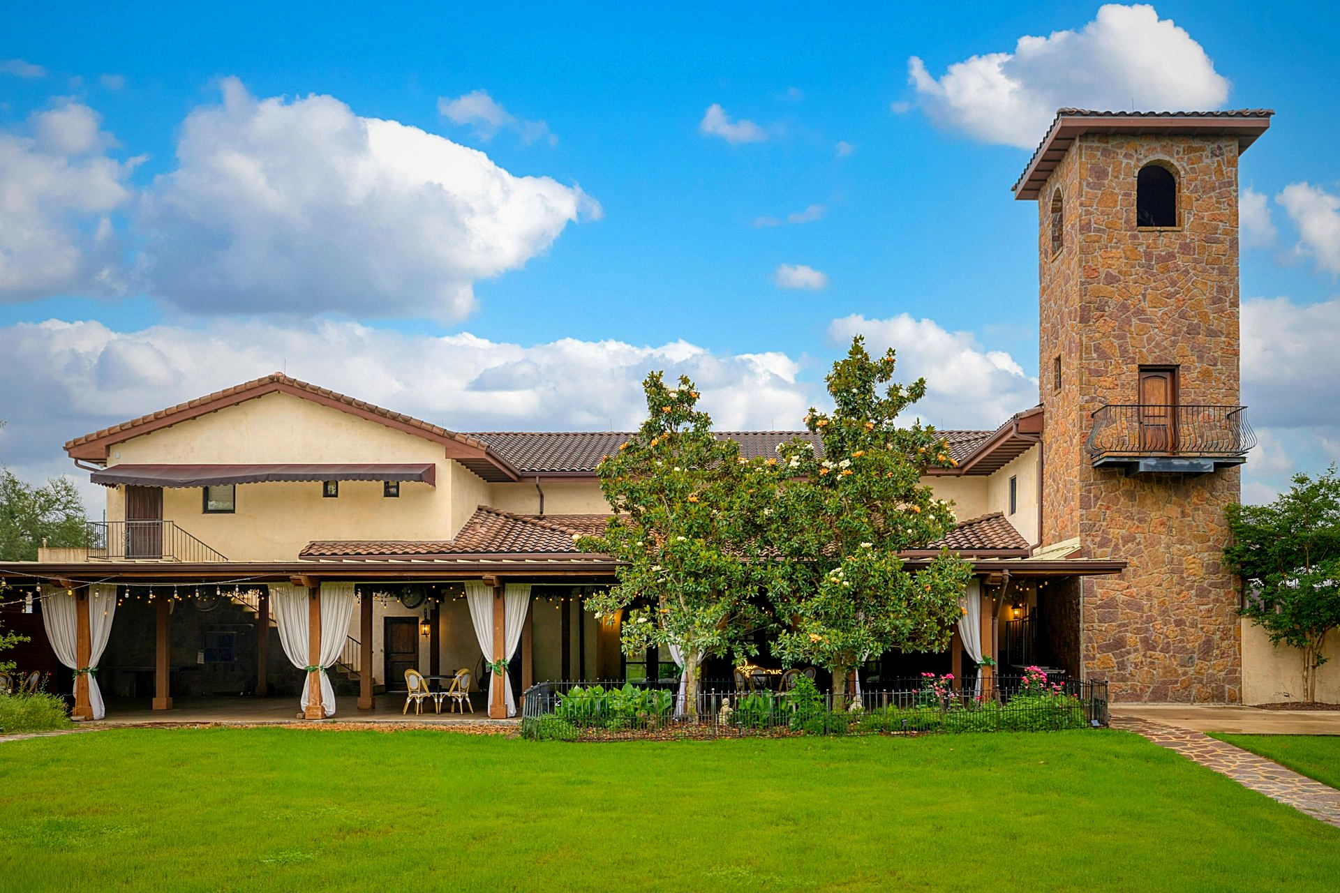 Mediterranean-style estate with stone tower, covered patio, lawn, and blue sky